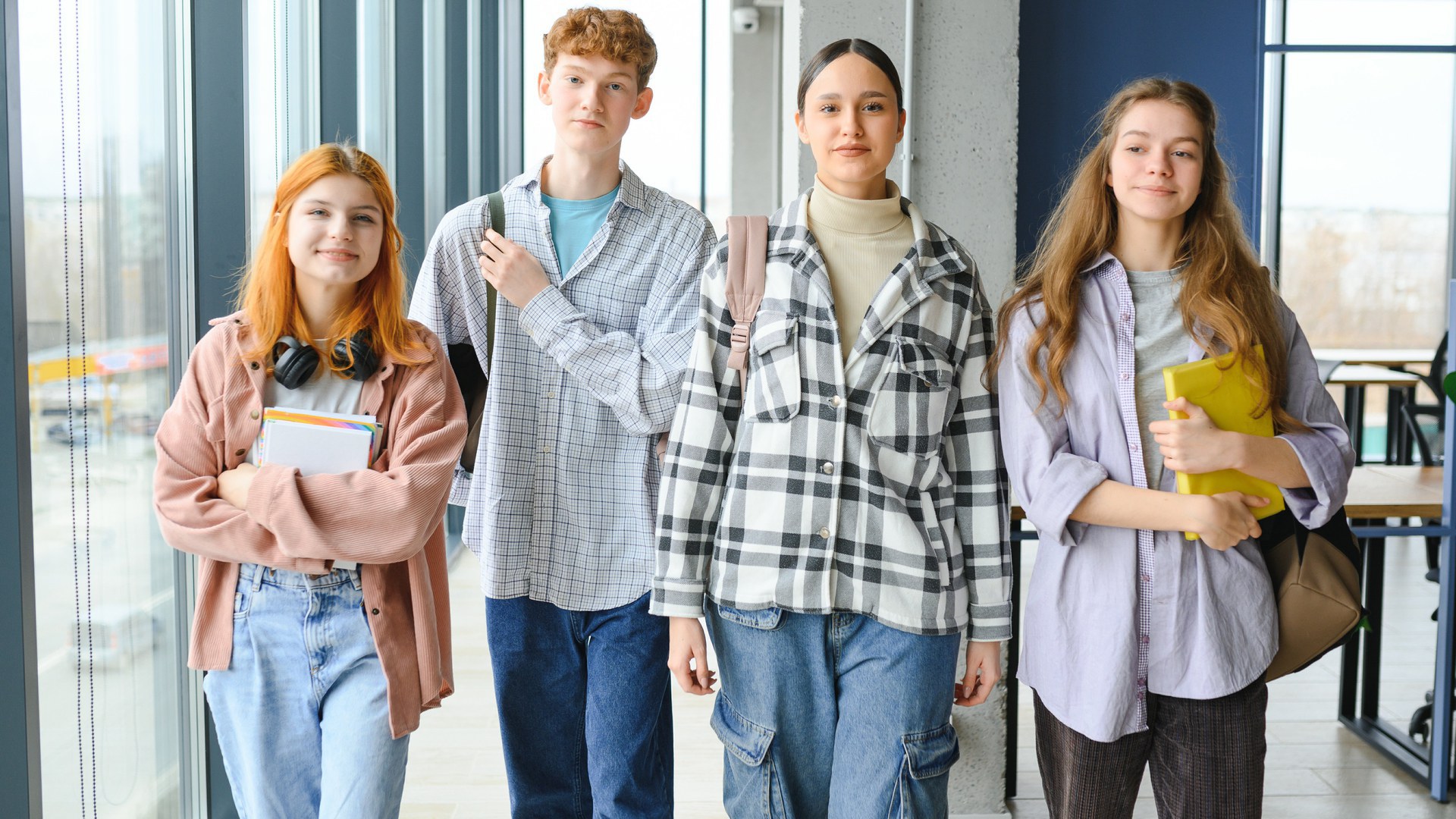 Vier zufriedene Maturanden laufen in einem Klassenzimmer auf die Kamera zu