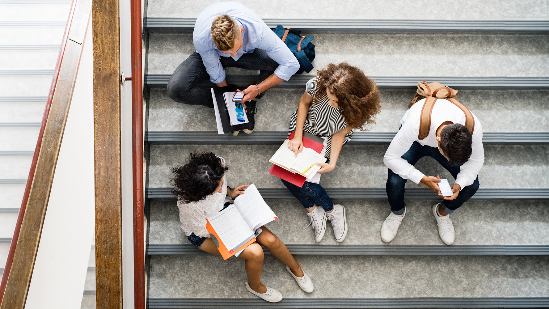 Blick von oben auf Gymnasiastinnen und Gymnasiasten, die auf der Treppe sitzen